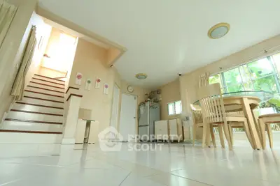 Spacious open-plan living area with dining set and staircase, featuring large windows for natural light.