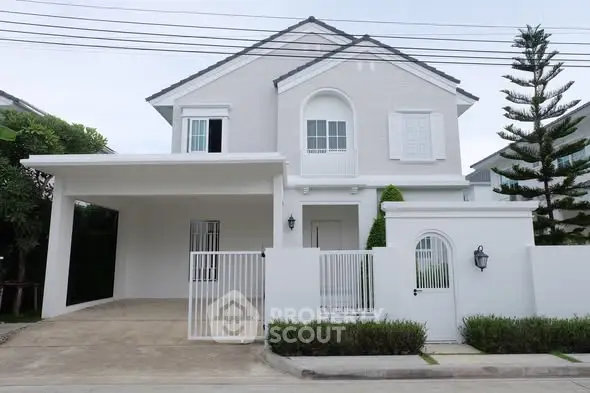 Elegant two-story white house with gated entrance and driveway, surrounded by lush greenery.