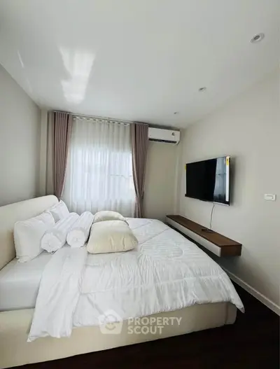Modern bedroom with cozy bed, wall-mounted TV, and elegant curtains in a bright, minimalist design.