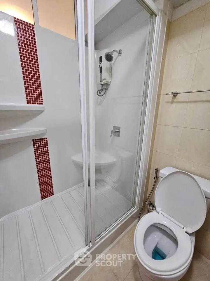 Compact bathroom with shower and toilet, featuring modern fixtures and red tile accents.