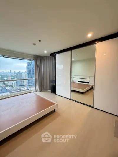 Spacious bedroom with city view and large mirrored closet in modern apartment.