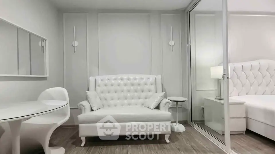 Elegant white living room with modern furniture and glass partition leading to bedroom.
