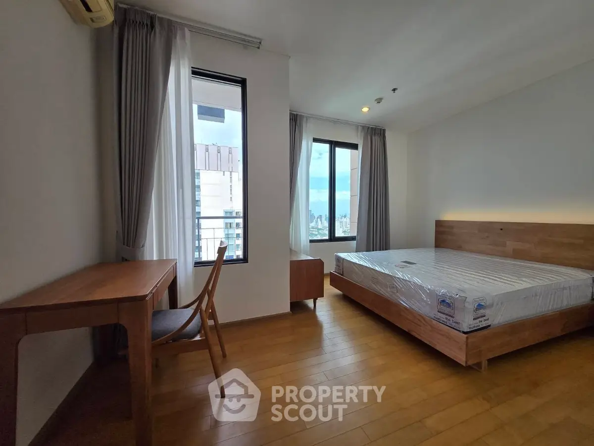 Spacious bedroom with wooden flooring and city view, featuring a modern bed and study desk.