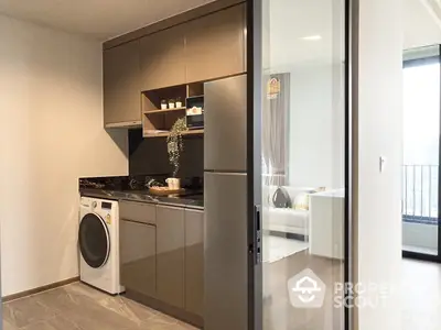 Modern kitchen with sleek brown cabinets, stainless steel appliances, and a washing machine, showcasing a functional urban living space with a glimpse of the balcony.