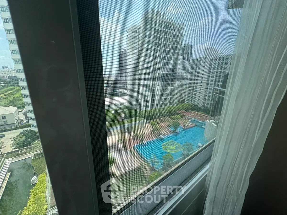 Stunning high-rise view with pool and cityscape from apartment window.