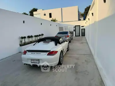 Modern driveway with luxury cars leading to a stylish white building entrance.