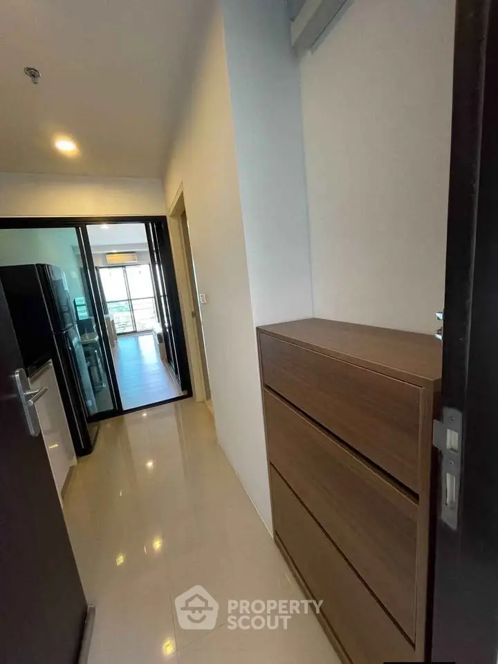 Modern apartment hallway with sleek storage and glass doors leading to a bright living area.