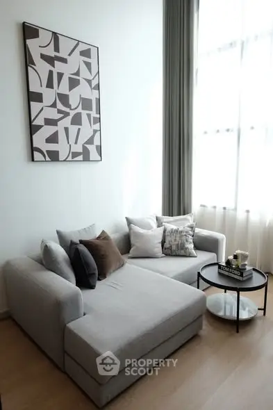 Modern living room with stylish gray sofa and abstract wall art, featuring floor-to-ceiling windows.