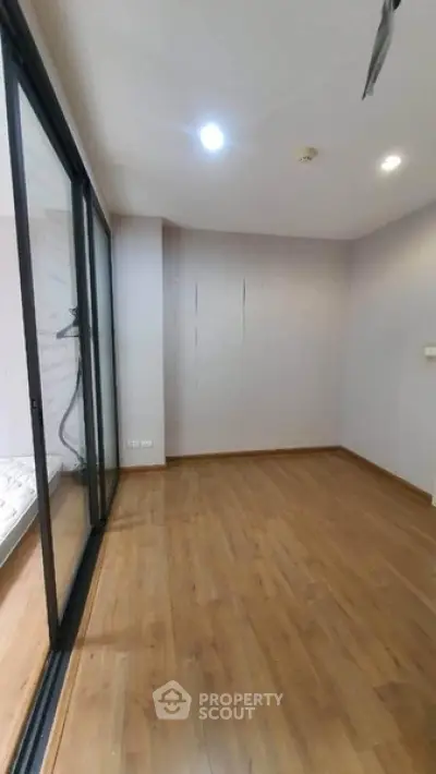Spacious empty room with wooden flooring and large glass doors leading to a balcony.