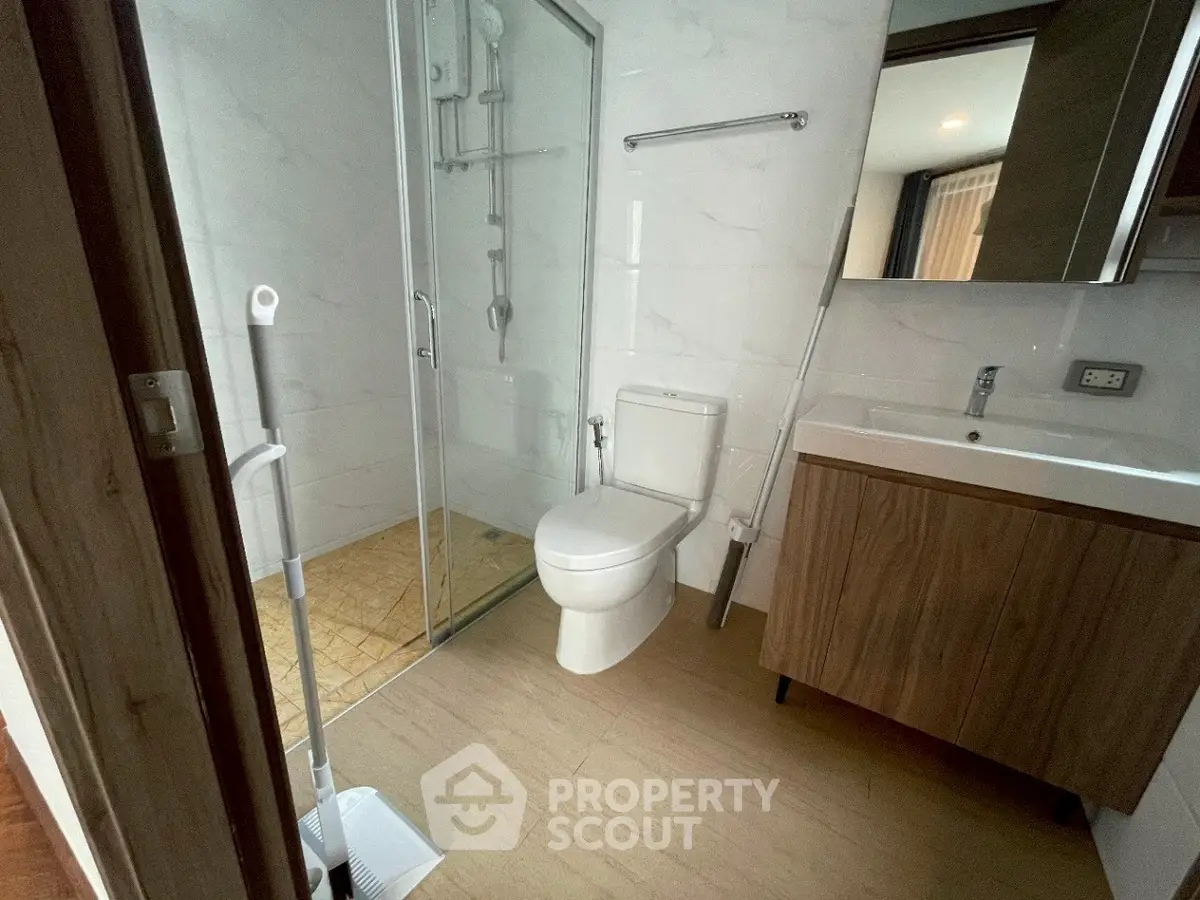 Modern bathroom with glass shower and wooden vanity in sleek apartment.