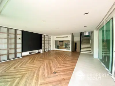 Expansive modern living room with herringbone wood flooring, large TV, and floor-to-ceiling windows leading to a bright, airy space.