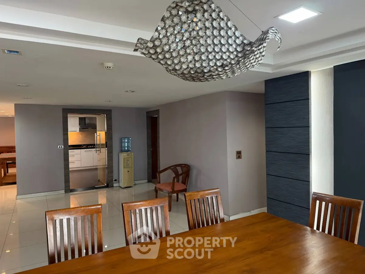 Spacious dining area with modern lighting and view into a sleek kitchen