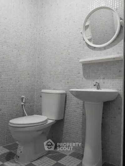 Modern bathroom with pedestal sink and round mirror in tiled interior.