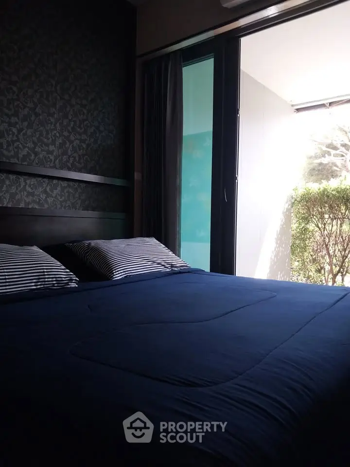 Cozy bedroom with large window and garden view, featuring elegant dark bedding and stylish wallpaper.
