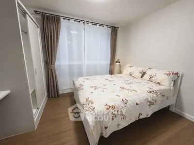 Cozy bedroom with floral bedding and large window, perfect for relaxation.