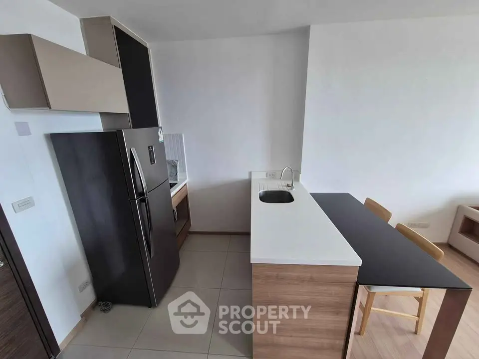 Modern kitchen with sleek black fridge and stylish breakfast bar in contemporary apartment.