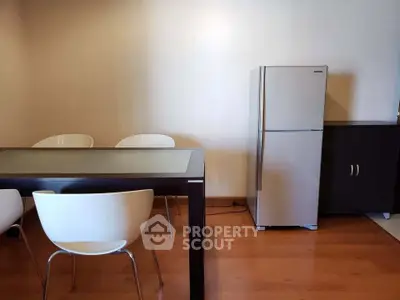 Modern dining area with sleek table, chairs, and stainless steel fridge in a cozy apartment.