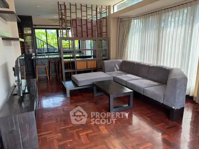 Spacious living room with elegant wooden flooring and modern furniture, featuring large windows for natural light.