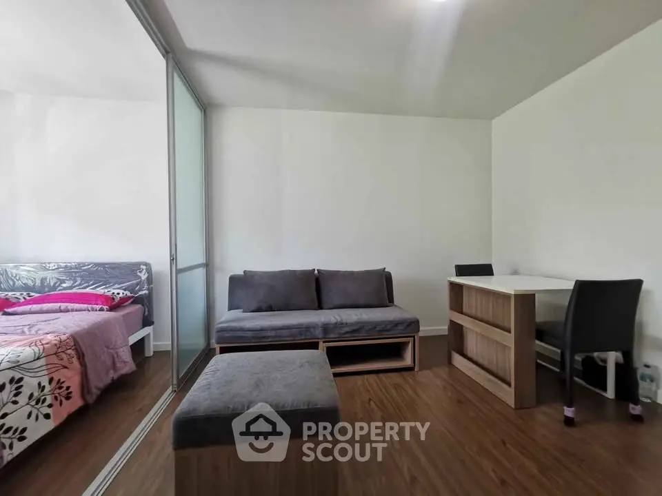Modern studio apartment with cozy living area and bedroom, featuring sleek furniture and wooden flooring.