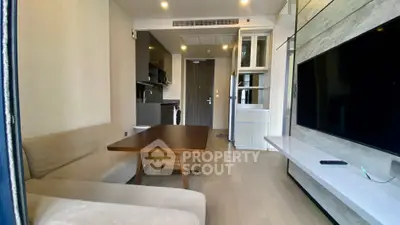 Modern living room with open kitchen, featuring sleek furniture and large TV.