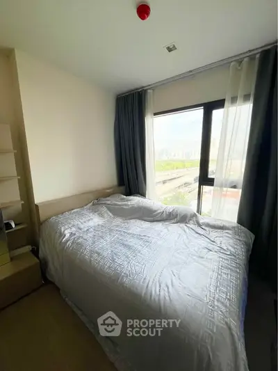 Cozy bedroom with large window offering city views, perfect for relaxation and comfort.