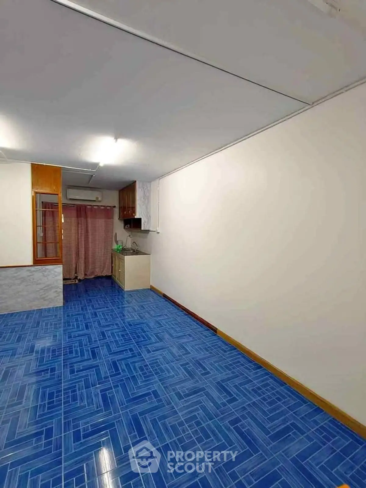 Spacious room with vibrant blue tiled flooring and compact kitchen area.