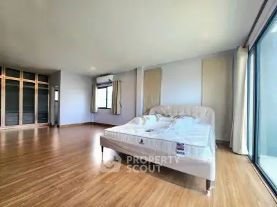 Spacious bedroom with large windows and wooden flooring in modern apartment.