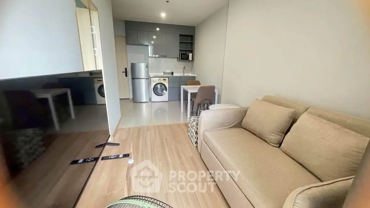 Modern living room with open kitchen, featuring a cozy sofa and sleek appliances.