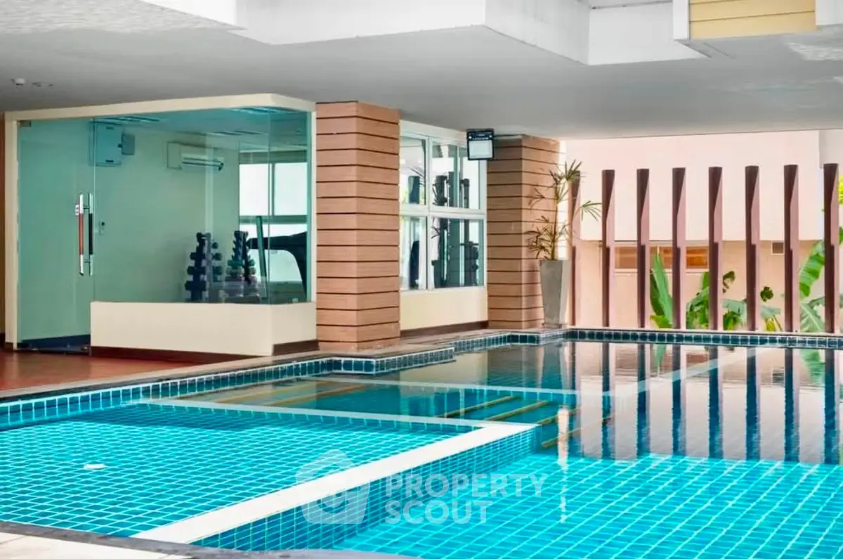 Luxurious indoor pool area with modern design and adjacent fitness room in upscale residential building.