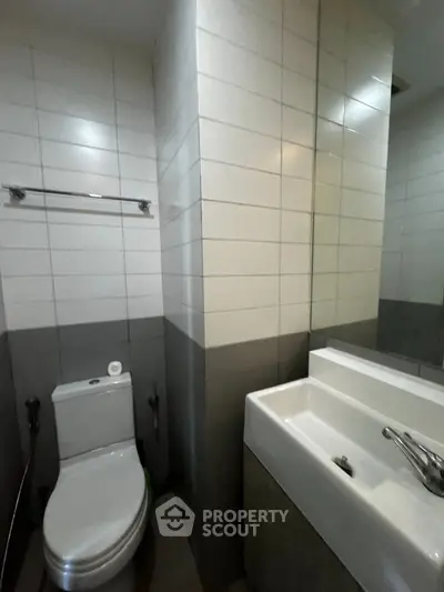 Modern bathroom with sleek design and tiled walls, featuring a toilet and a stylish sink.