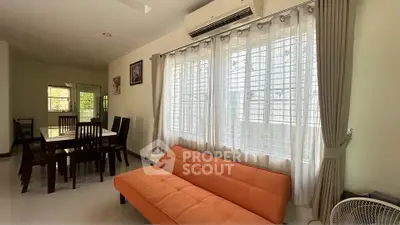 Spacious living room with bright orange sofa and dining area, featuring large windows and air conditioning.