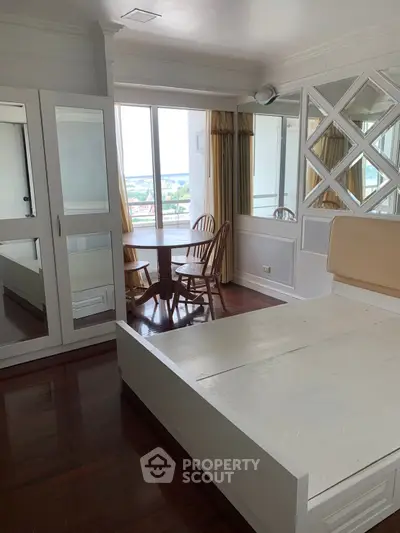 Spacious bedroom with mirrored wardrobe and balcony view, featuring elegant wooden flooring and natural light.