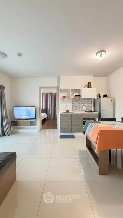 Modern open-plan living room with kitchen and dining area, featuring sleek furniture and tiled flooring.