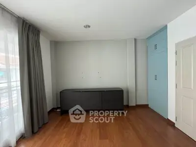 Spacious bedroom with wooden flooring and large window for natural light.