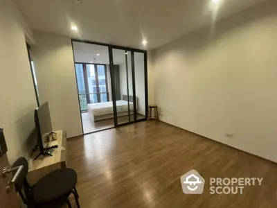 Modern apartment with spacious living area and glass partitioned bedroom, featuring wooden flooring and natural light.