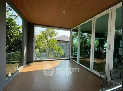 Spacious balcony with glass doors and wooden ceiling, offering a serene view of greenery and modern architecture.