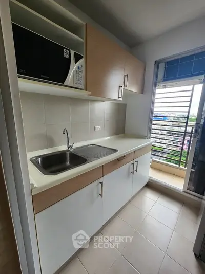 Modern kitchen with sleek cabinetry and balcony view, featuring a built-in microwave and stainless steel sink.