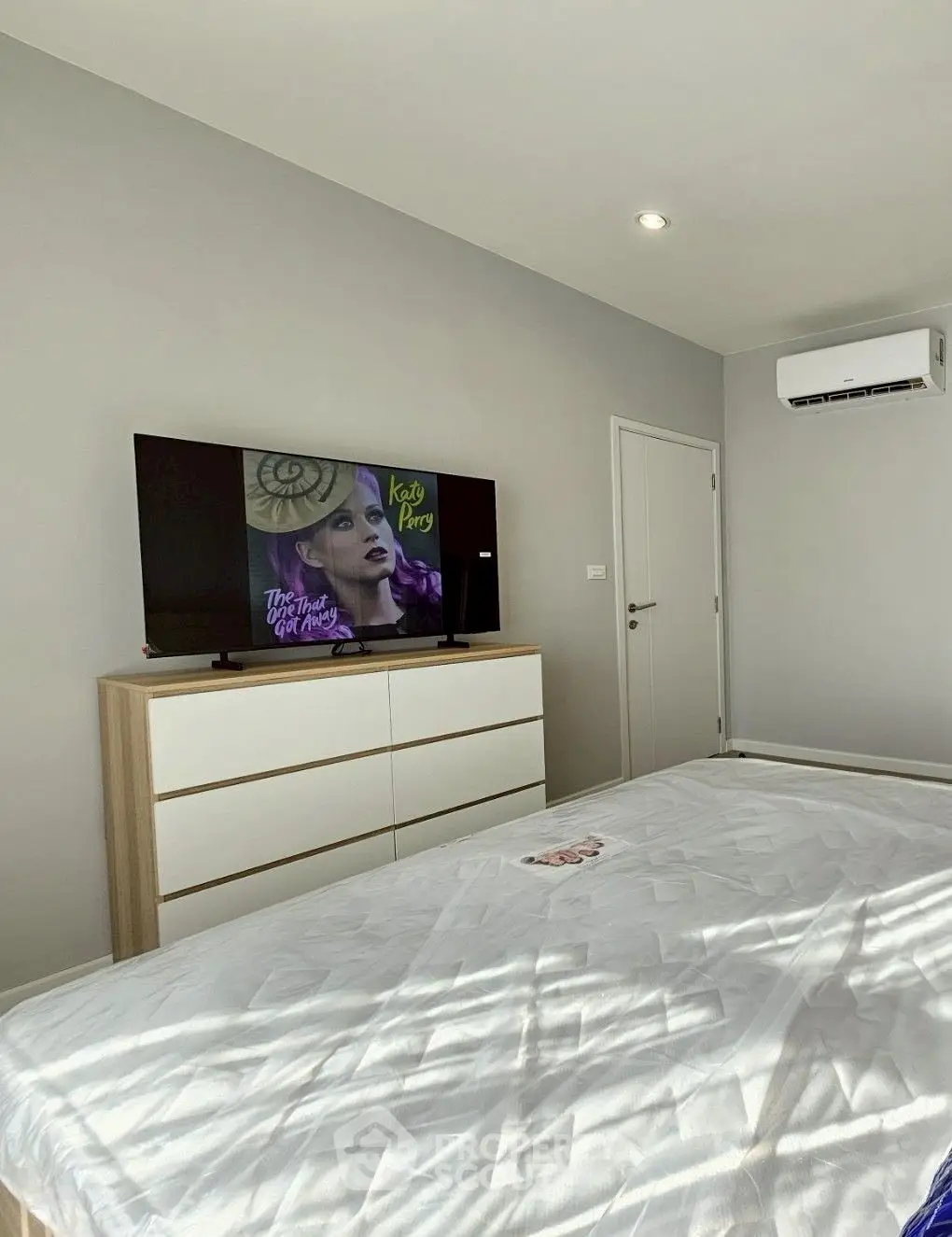 Modern bedroom with sleek furniture and wall-mounted TV, featuring a minimalist design and air conditioning.