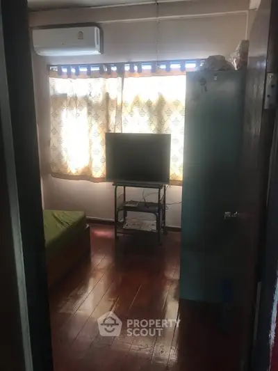 Cozy small bedroom with wooden floors, air conditioning, and natural light through patterned curtains.