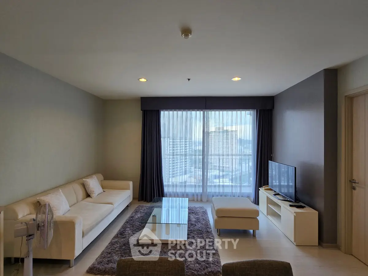 Spacious modern living room with large window offering city view, featuring cozy sofa and sleek TV setup.