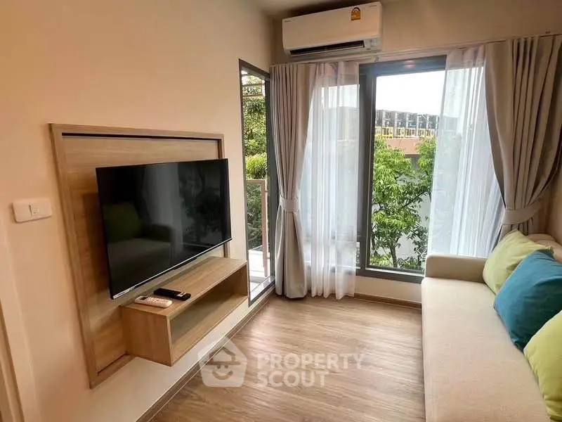Cozy living room with large window and modern decor, featuring a wall-mounted TV and air conditioning.