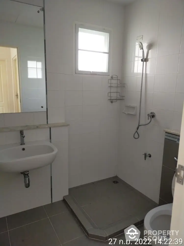 Pristine white-tiled bathroom featuring a walk-in shower, pedestal sink, and a large mirror reflecting a bright interior.