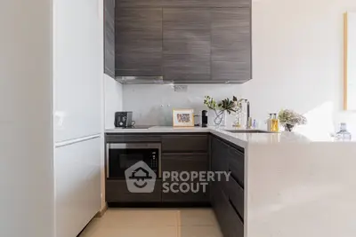 Modern kitchen with sleek dark cabinets and integrated appliances in a bright, stylish apartment.