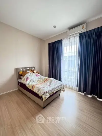 Cozy bedroom with single bed and large window, featuring wooden flooring and modern air conditioning.
