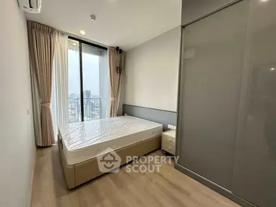 Modern bedroom with large window and city view, featuring a comfortable bed and sleek wardrobe.