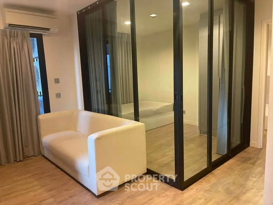 Modern apartment with glass-enclosed bedroom and cozy living area, featuring sleek wooden flooring and neutral decor.