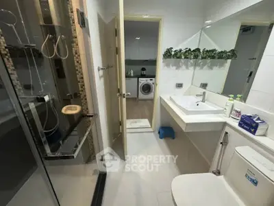 Modern bathroom with sleek fixtures and view into laundry area with washing machine.