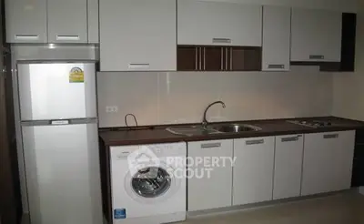Modern kitchen with sleek cabinets, washing machine, and compact fridge.