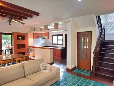 Charming open-layout living room with modern kitchen and wooden staircase in cozy home.