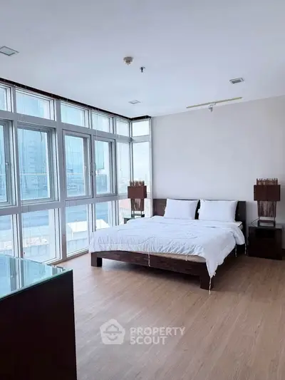 Spacious bedroom with large windows and modern furnishings in a high-rise apartment.